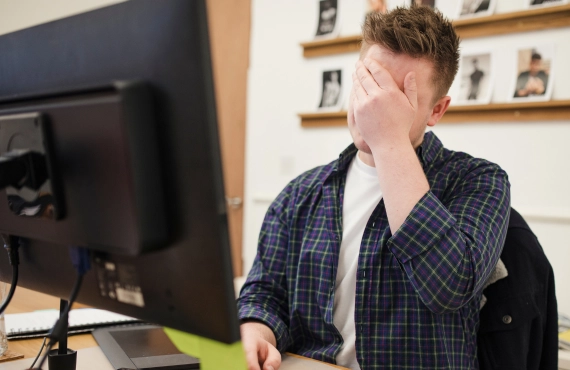 Man Covering His Face in Front of a Computer after Making a Mistake